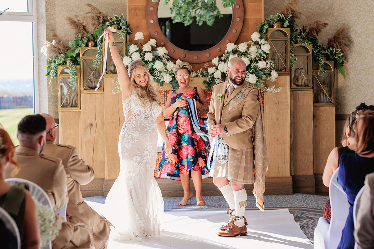 Bride and groom celebrating during their indoor wedding ceremony at The Waterside Hotel, with floral arrangements behind them.