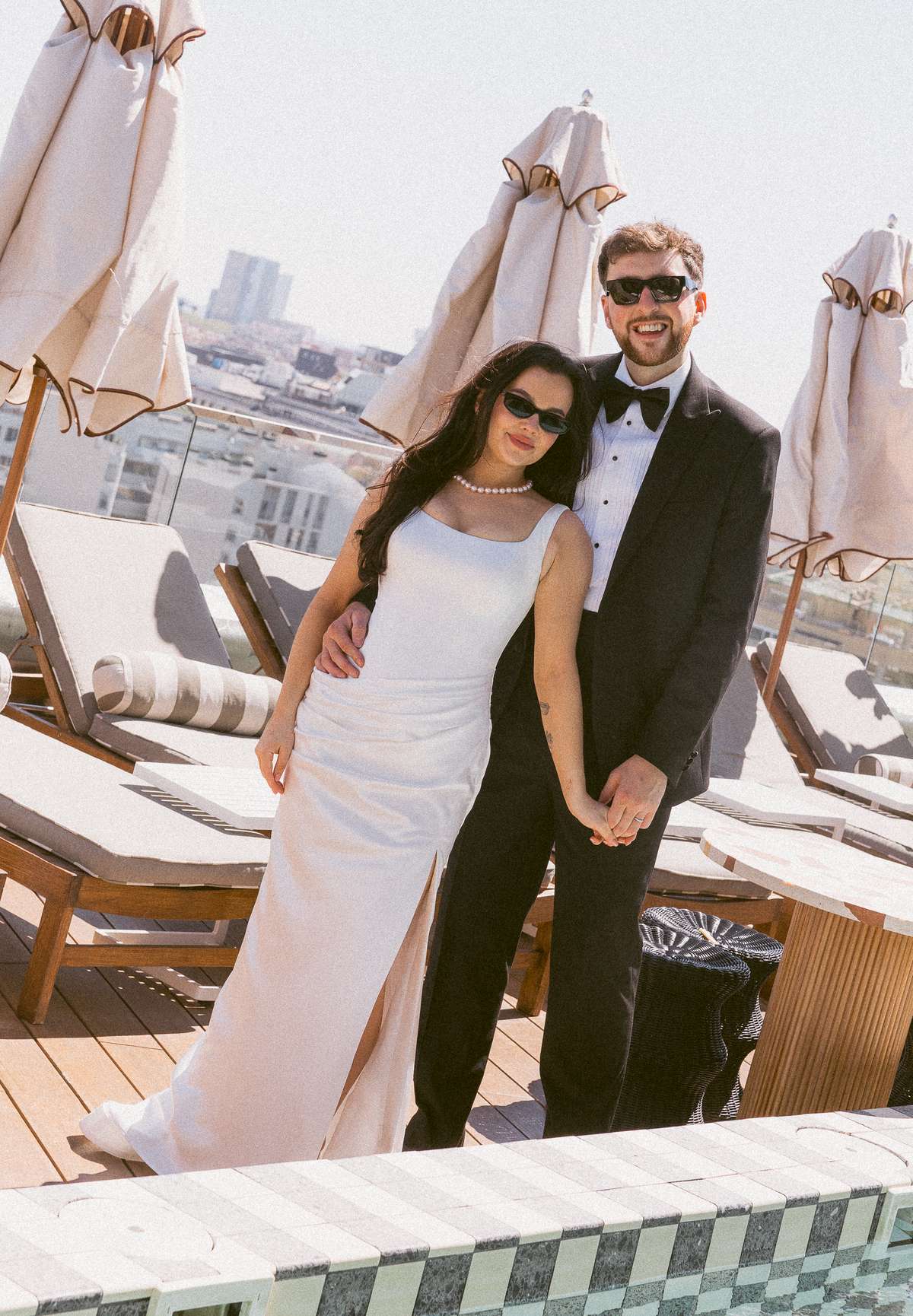 Bride and groom wearing sunglasses pose together on the rooftop at The Hoxton Barcelona during their destination wedding celebration.