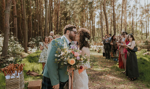 couple kissing after getting married - bride holding colourful floral bouquet