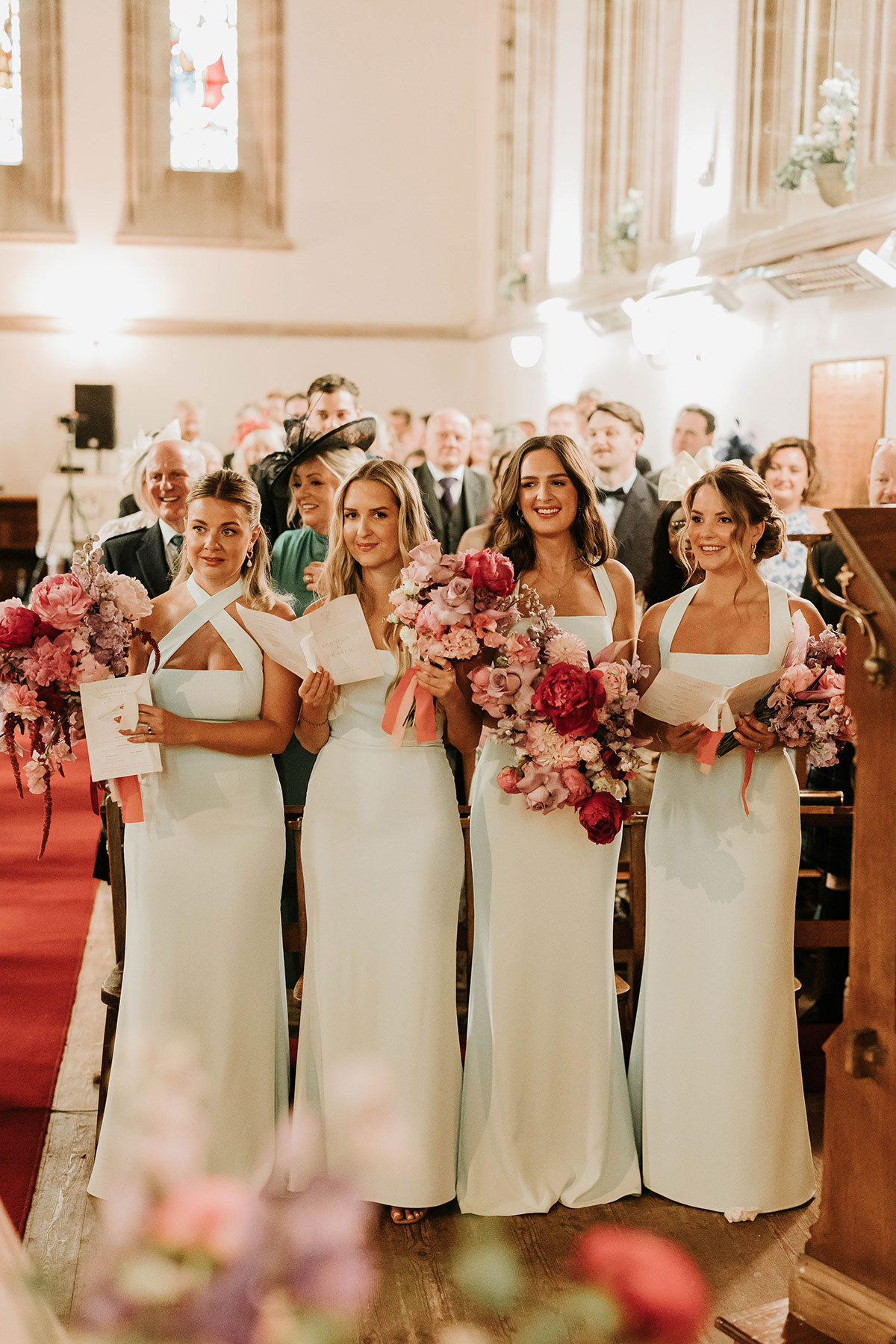 Bridesmaids in pale green dresses holding pink and red bouquets during Drumtochty Castle Aberdeenshire wedding ceremony