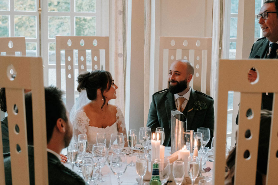 Bride and groom smile at each other while sitting at table