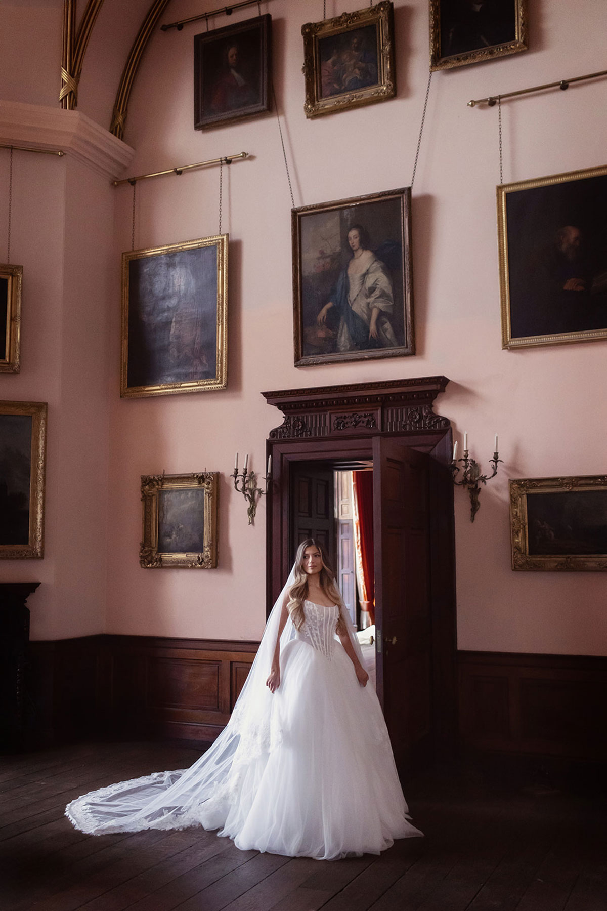 Bridal model in a full wedding dress and veil beneath framed portraits at Gosford House.