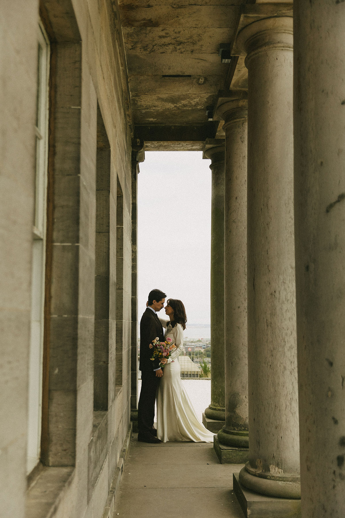 Bride and groom posing between stone pillars at the City Observatory wedding venue in Edinburgh.