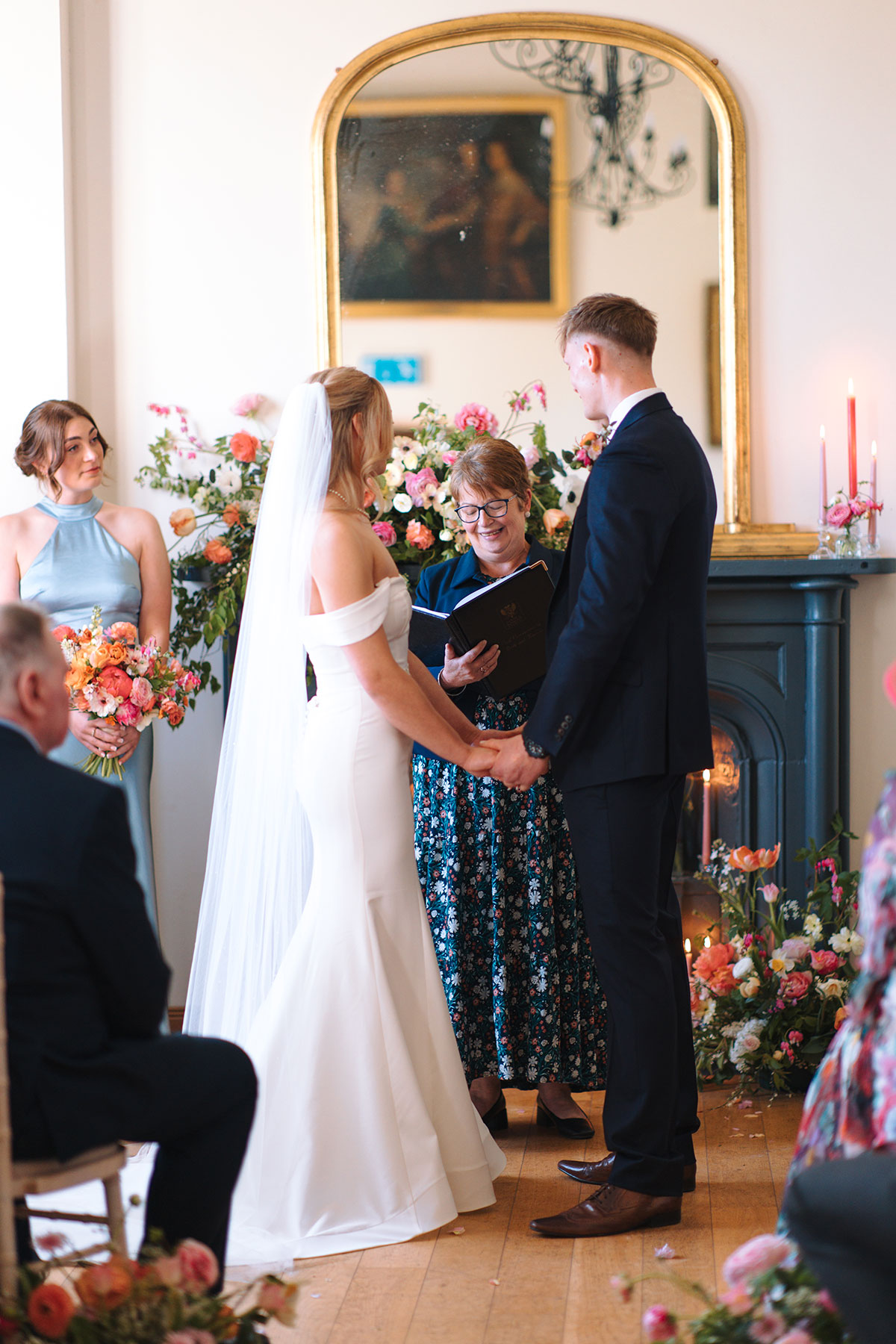 Couple exchanging vows in front of fireplace with floral arrangements during wedding ceremony