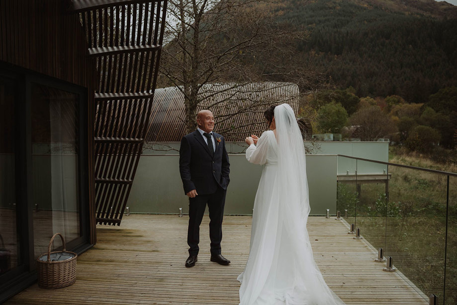 a bride and a man in a suit on a wooden deck with glass panels