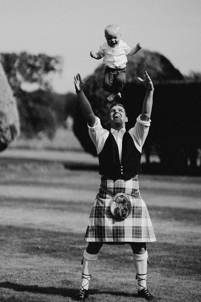 A black and white photo of a man in a kilt throwing a small child into the air above his head