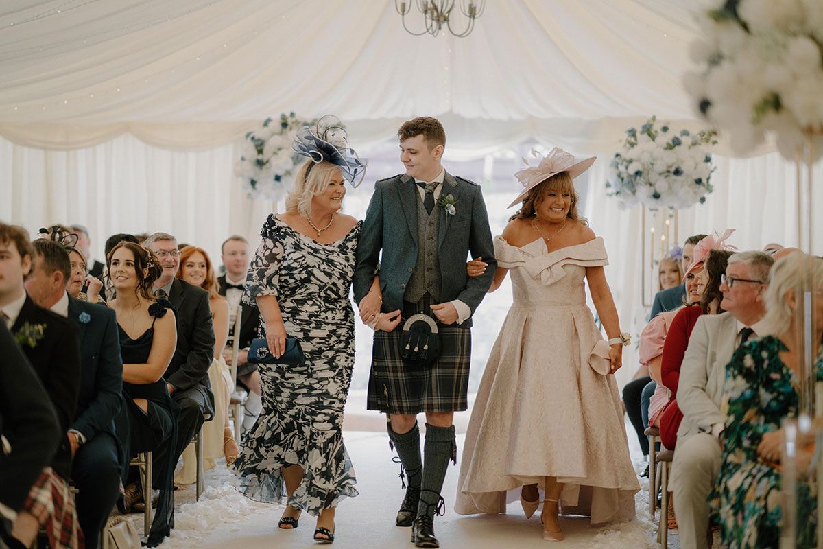 groom walks down the aisle with two women linking his arms either side during wedding at cornhill castle