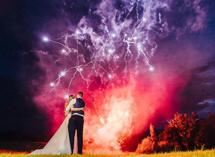 A ground-level view of the bride and groom watching red and purple fireworks