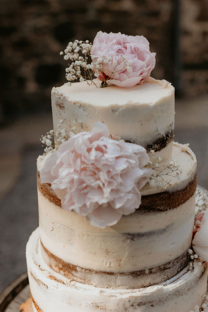 a close up of an ivory buttercream wedding cake with pink peony and gypsophila flower decoration