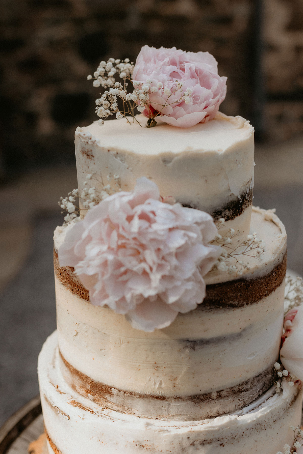 a close up of an ivory buttercream wedding cake with pink peony and gypsophila flower decoration