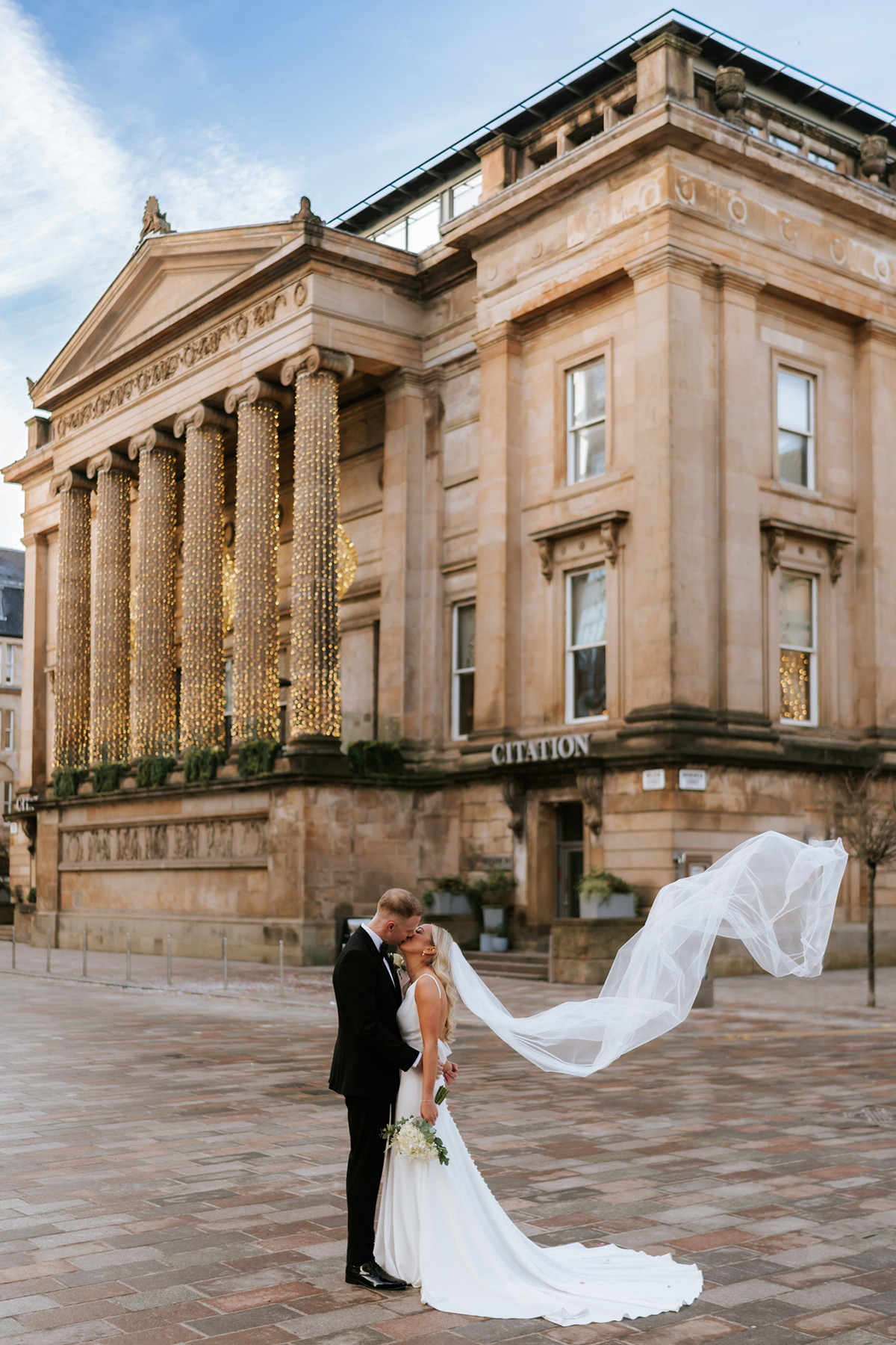 Newlywed couple outside Citation wedding venue in Glasgow with flowing veil and grand sandstone exterior