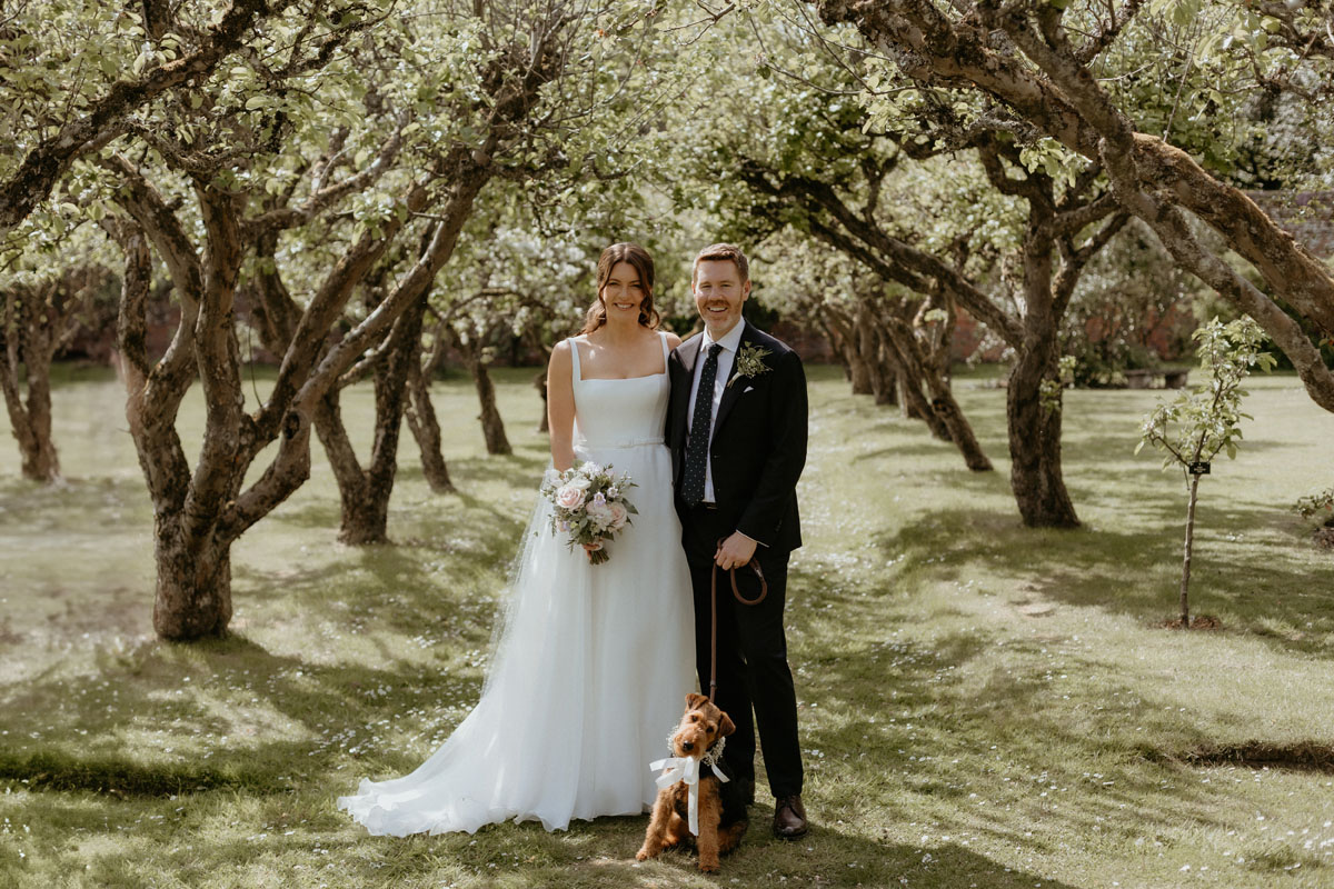 Newlyweds posing with their dog in the orchard at The Byre at Inchyra in Perthshire.