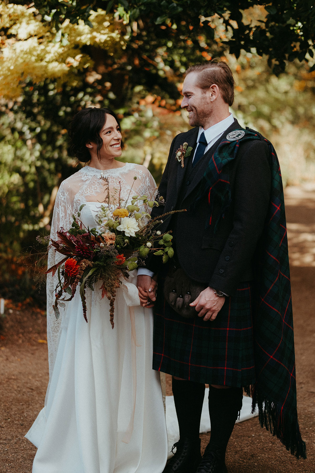 Bride and groom smile at one another during their first look at Cambo Country House, surrounded by autumn foliage.