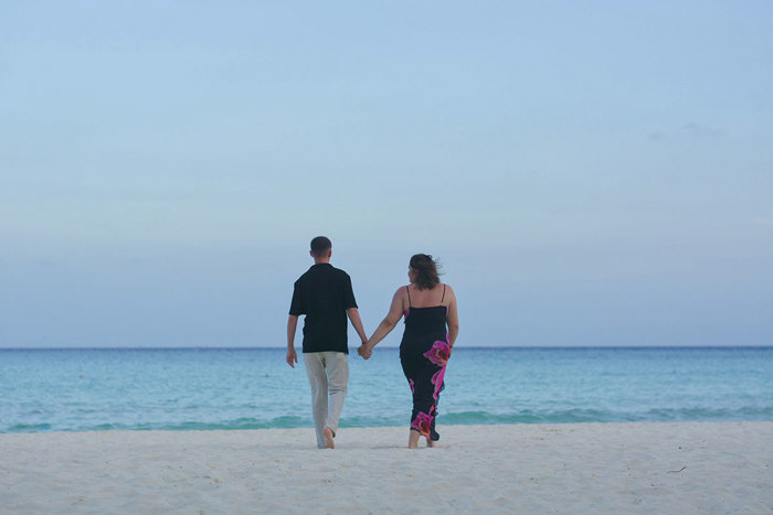 two people holding hands walking on a beach.