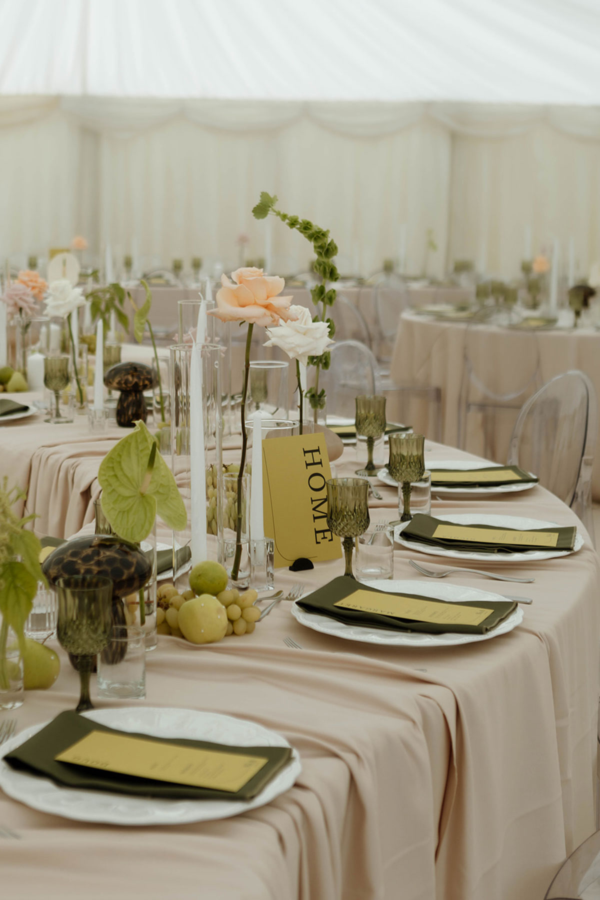 Serpentine reception table in a marquee with blush linens, green glassware and floral centrepieces.