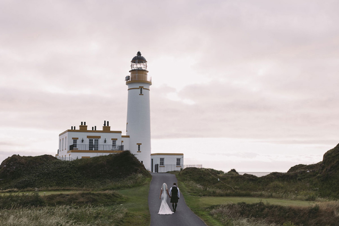 Bride And groom walk towards the lighthouse