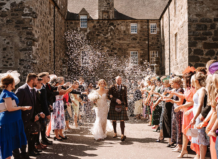 two long rows of people shower a bride and groom with confetti outside the Barn at Barra Castle