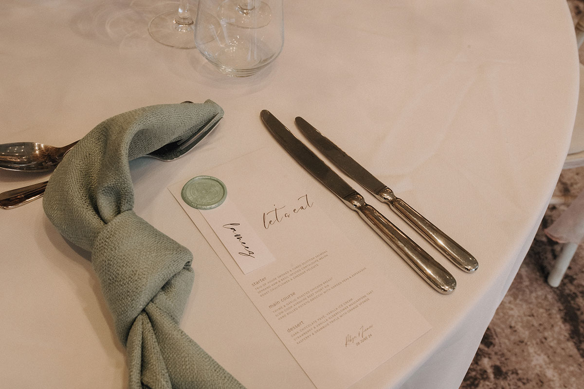 a table set with silver cutlery, a printed script menu and knotted green napkin