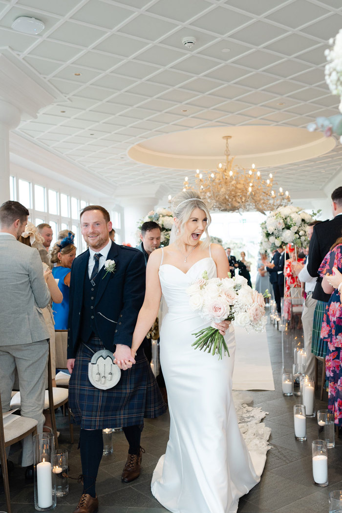 an elated bride and groom walking hand in hand up the aisle at the Conservatory at the Old Course Hotel.