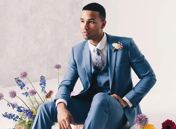 man sitting in blue suit with patterned tie surrounded by flowers
