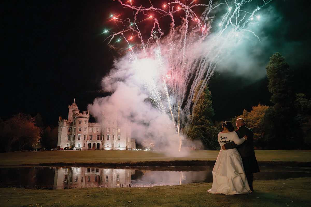 Bride and groom watching fireworks reflected in the pond outside Cluny Castle during their evening celebrations.