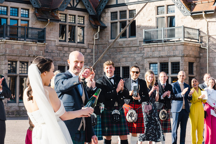 Groom opening a bottle of champagne with a sword