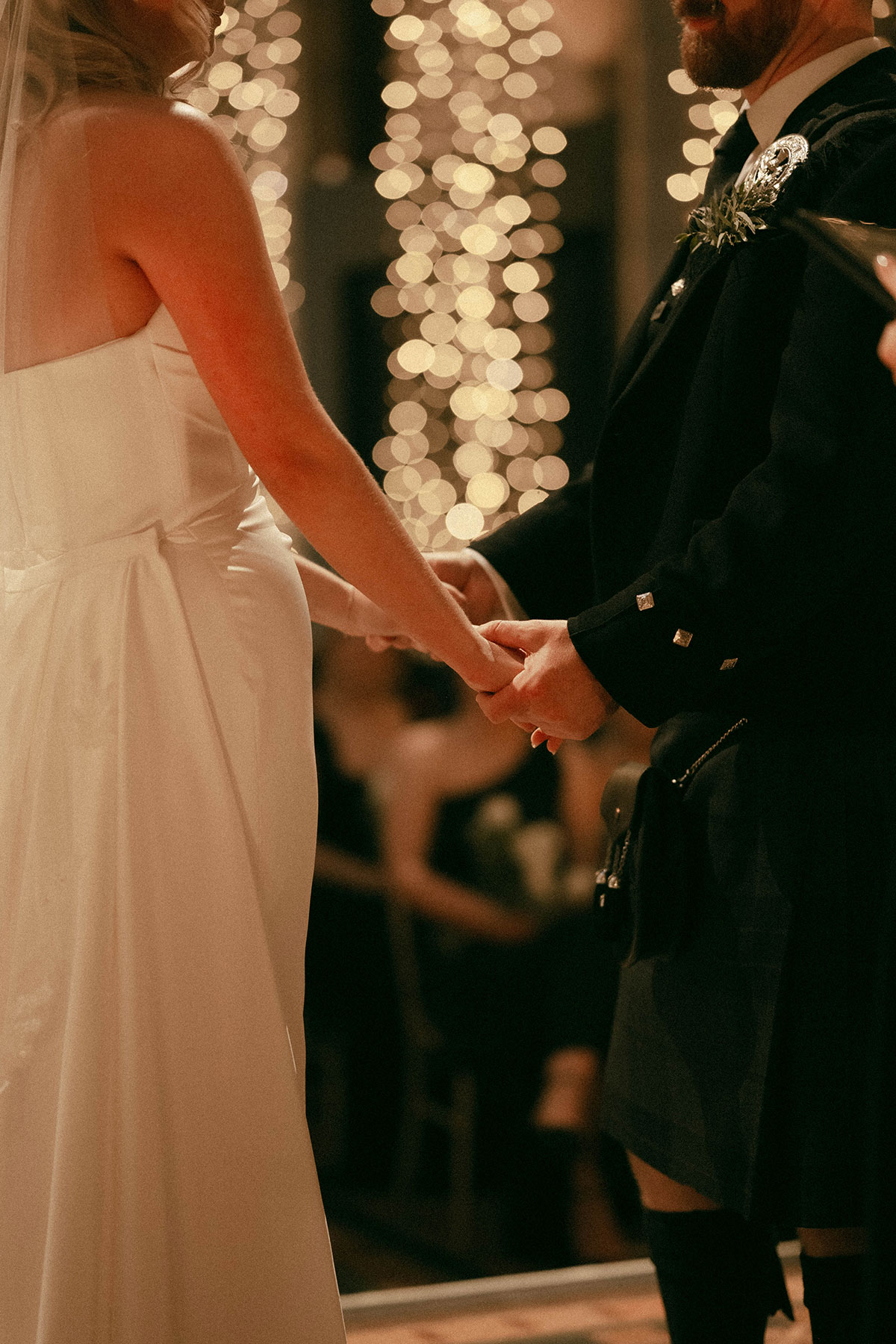 close up of couple holding hands during wedding ceremony with fairy light backdrop