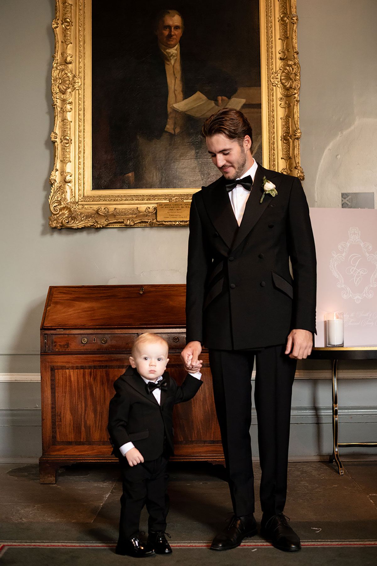 Groom holding toddler’s hand in matching tuxedos at Signet Library wedding