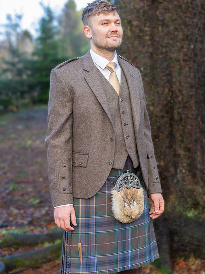 A man wearing a purple and brown kilt with a brown jacket and waistcoat 