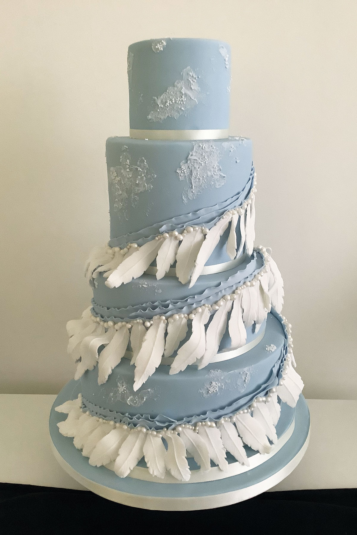 Unique blue four-tier wedding cake decorated with white feathers, pearls and textured icing, designed by Infinite Indulgence in Troon