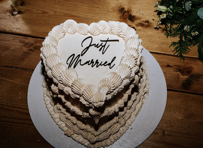 a heart shaped white wedding cake with ornate piping that reads 'Just Married'