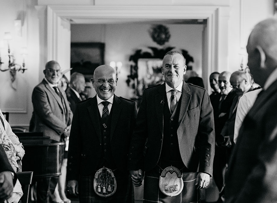 two smiling grooms walking down an aisle while holding hands