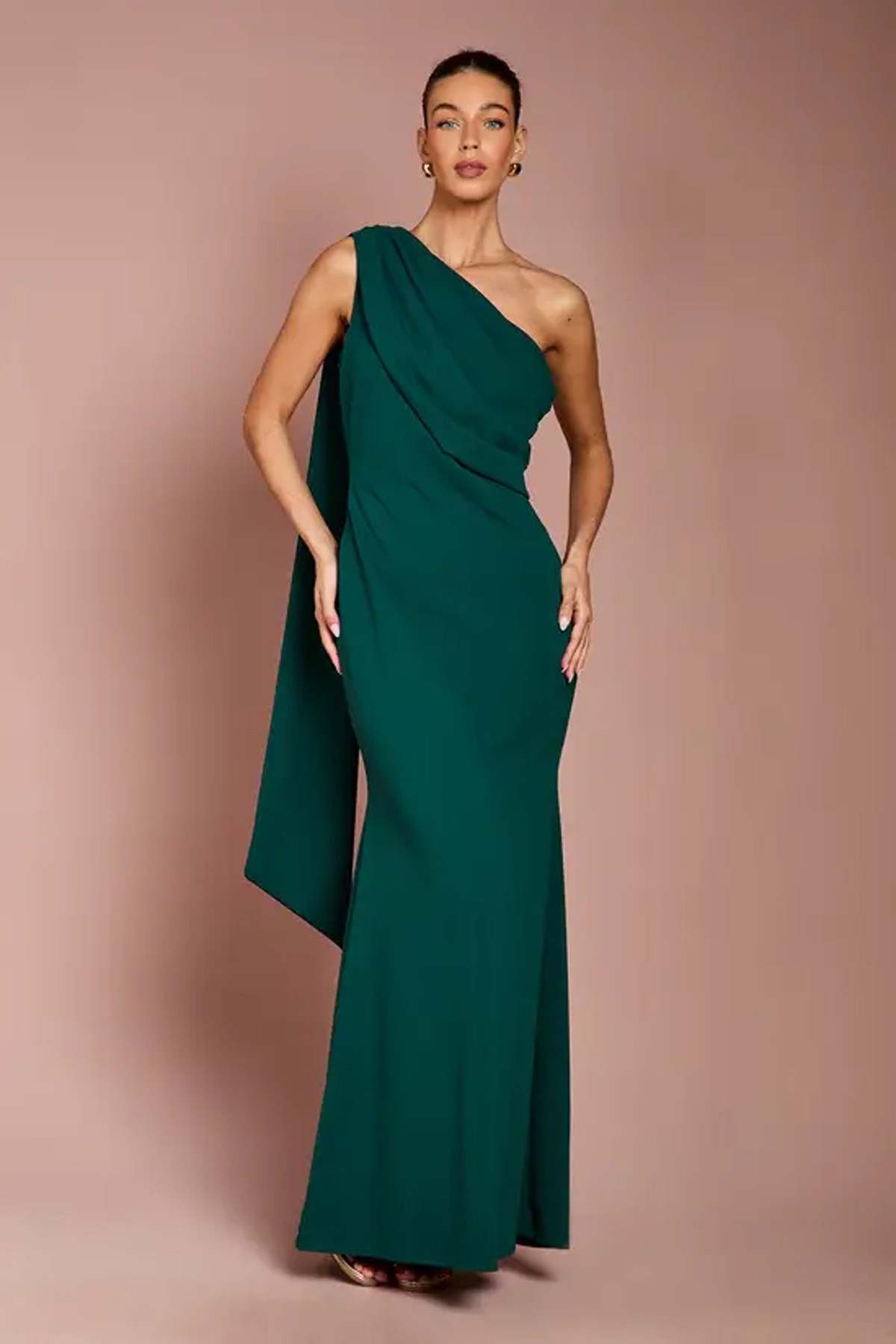 Woman wearing an emerald-green one-shoulder crepe maxi dress with draped detailing and a floor-length skirt.