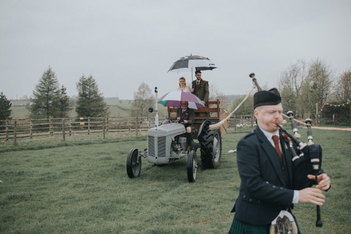 Couple ride a tractor as a bagpiper walks in front of them