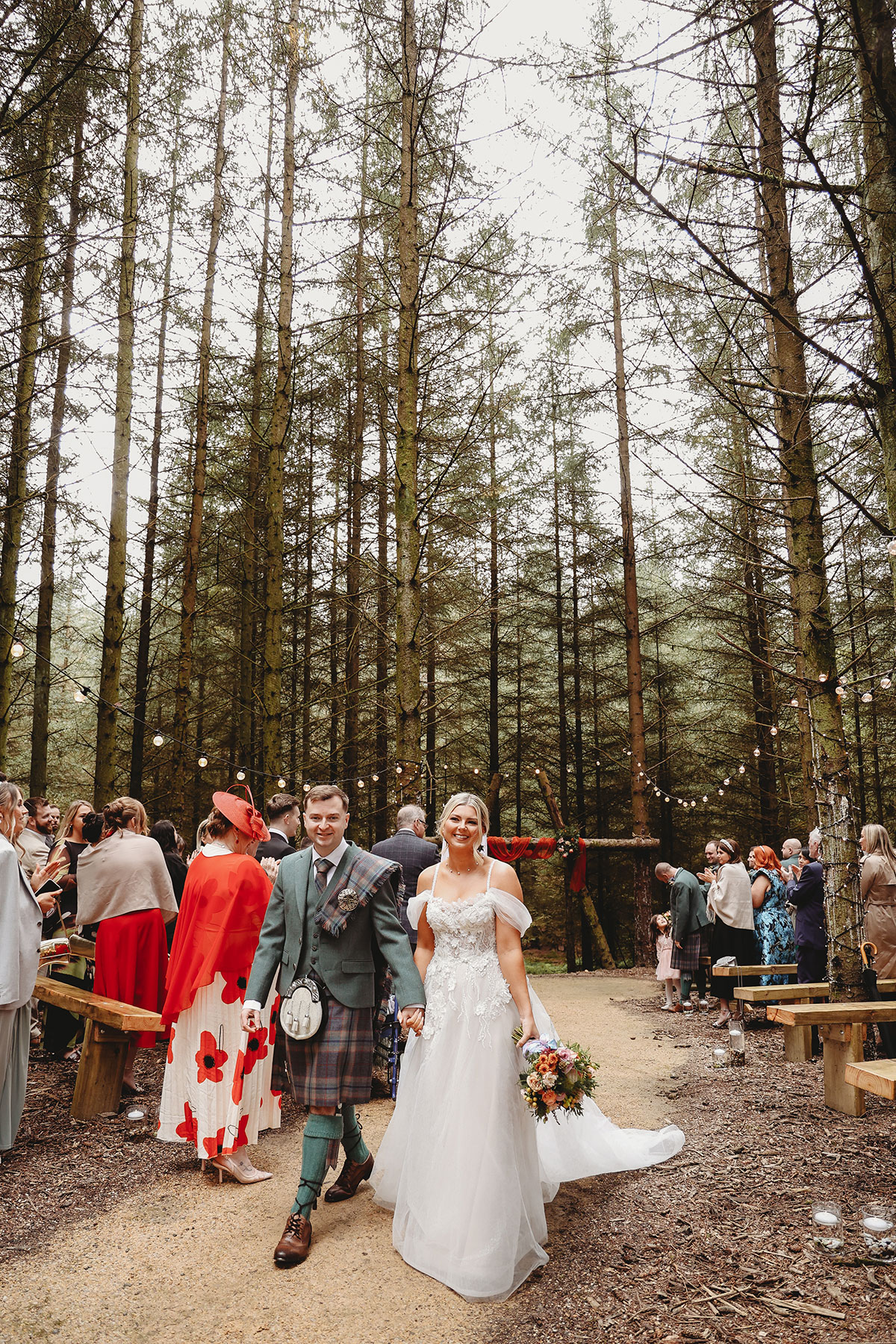 Newlyweds walking back down the aisle after their woodland wedding ceremony surrounded by family and friends
