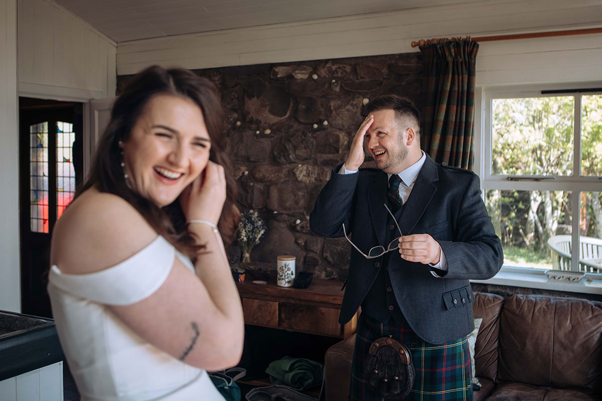 Bride and groom laugh together while getting ready inside their Highland accommodation before their Achnahaird Bay elopement.