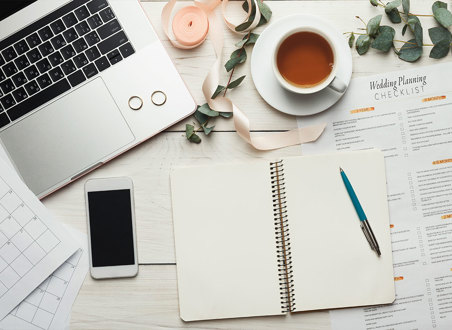 books phone and notepad strewn across desk with laptop