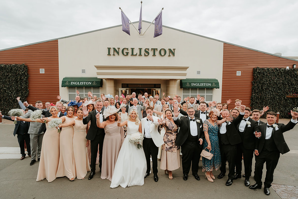 Group wedding photo outside Ingliston Country Club with bride, groom and guests celebrating in Renfrewshire