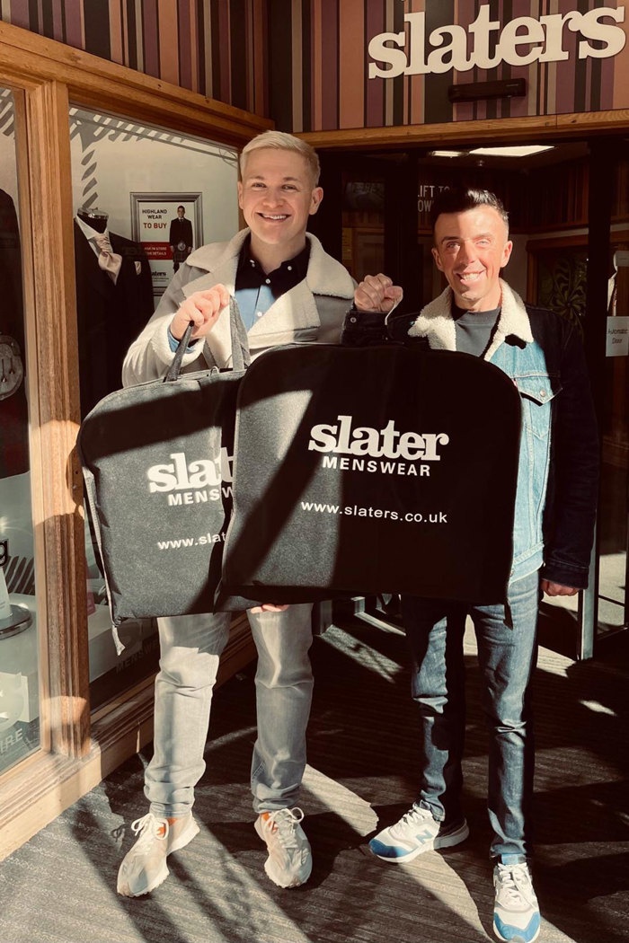 two men holding Slater Menswear suit bags outside Slater Menwear