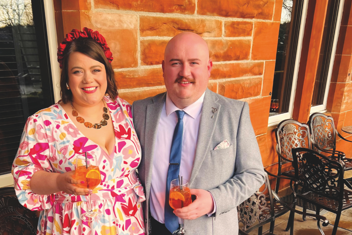 Man and woman in formal attire smiling holding orange drinks