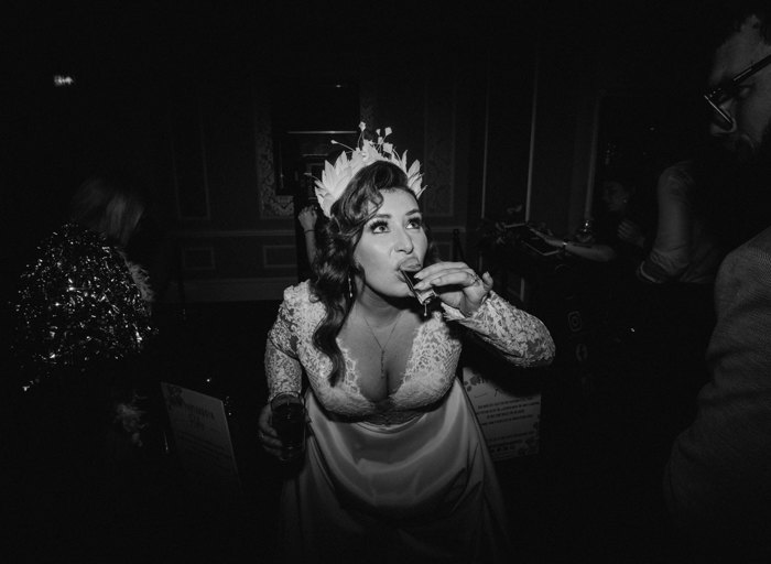 a black and white photo of a bride wearing a lace dress and a feather headband taking a shot