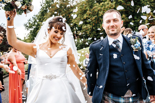 bride and groom walk towards camera smiling while their guests throw white coloured confetti on them
