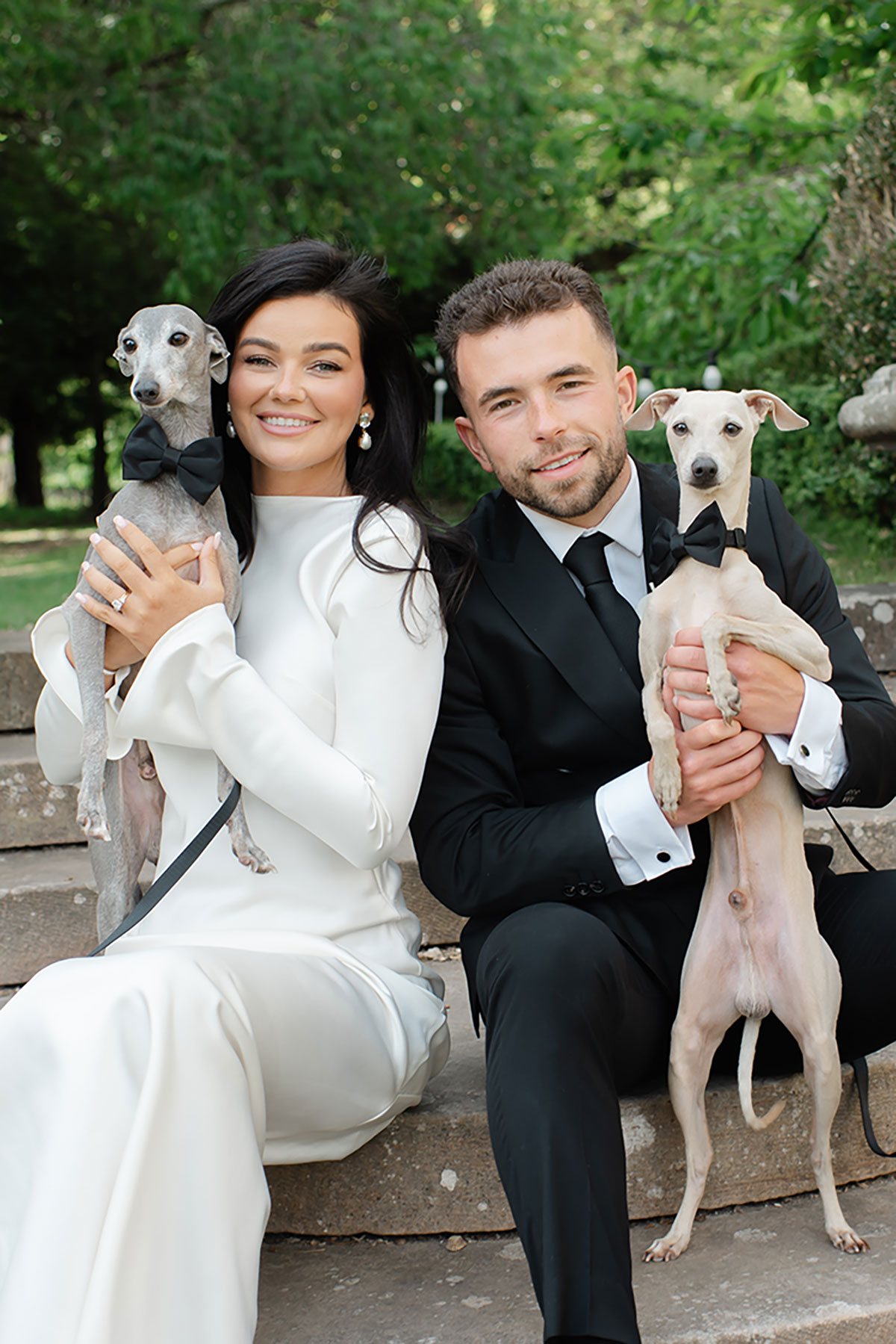 Bride and groom sitting on stone steps at Carberry Tower holding their two dogs wearing black bow ties