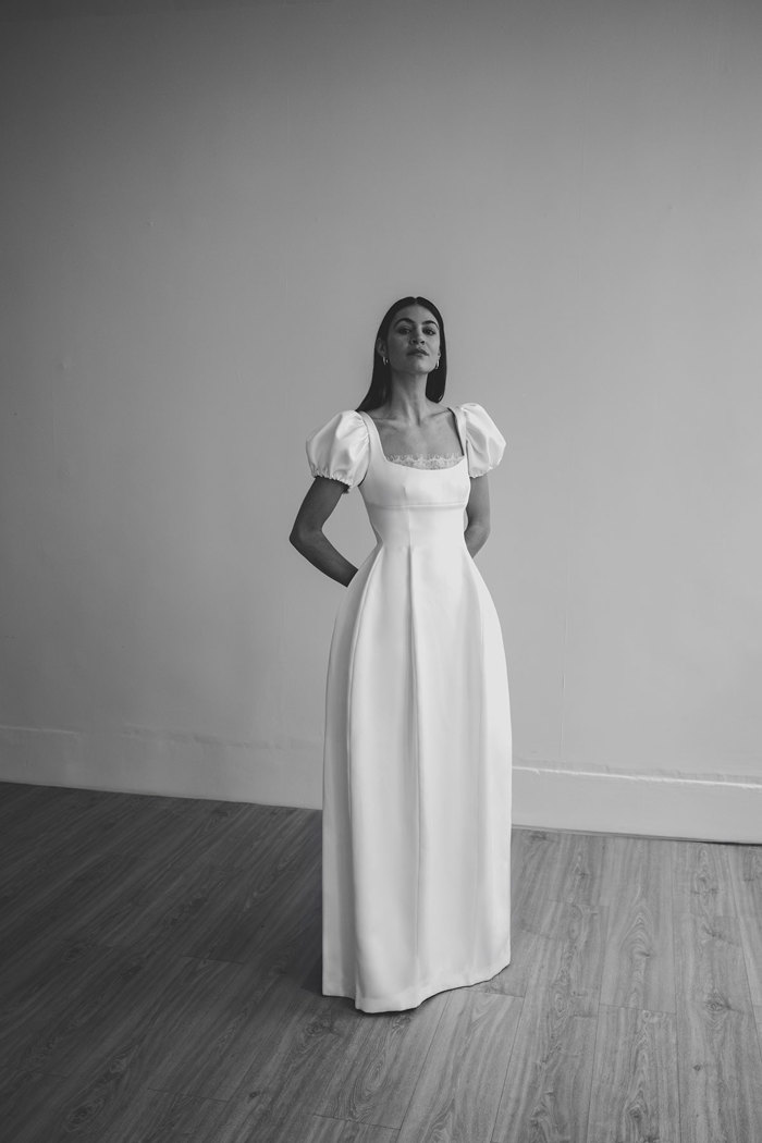 a black and white image of a dark haired woman in a formal white wedding dress with puffed sleeves and a lace-lined neckline