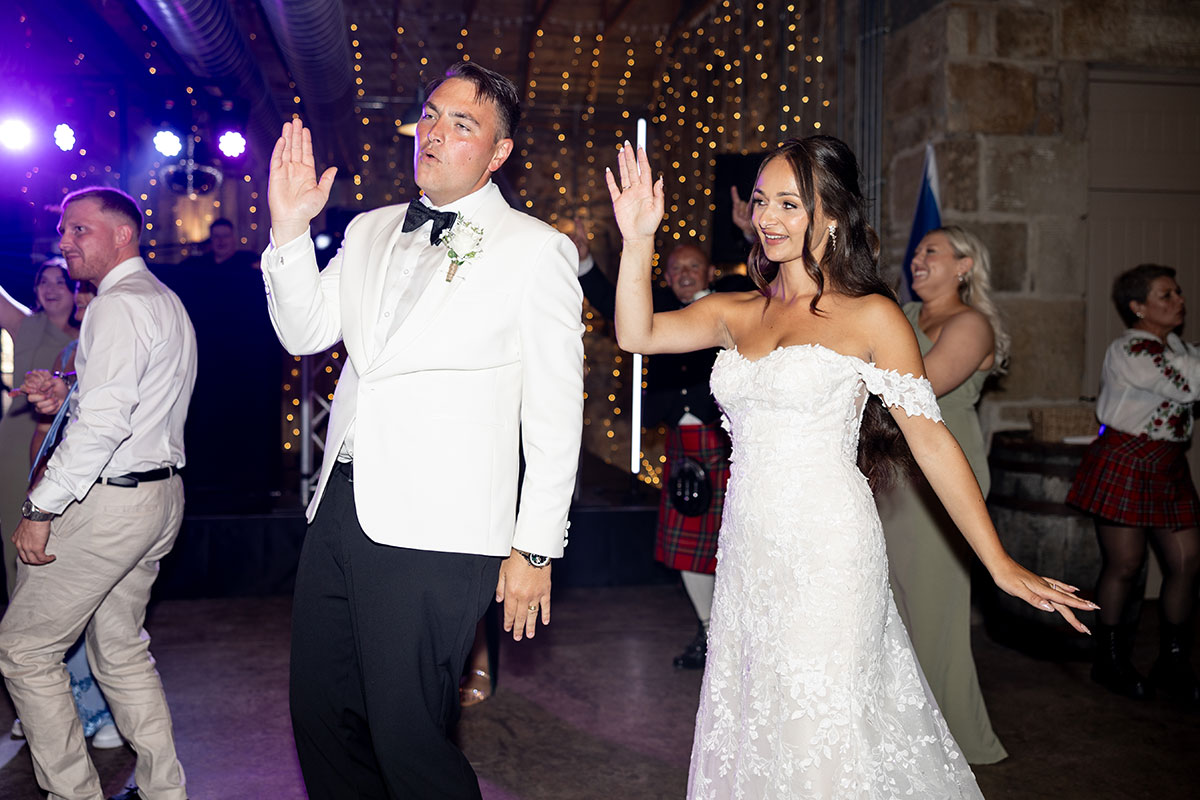 Newlyweds dance under warm string lights during evening party at Falside Mill wedding reception