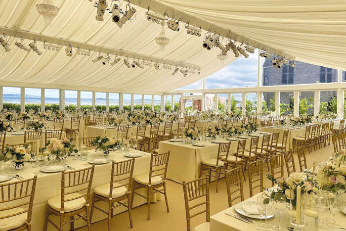 A large permanent marquee with multiple rows of dining tables with white linens and floral arrangements