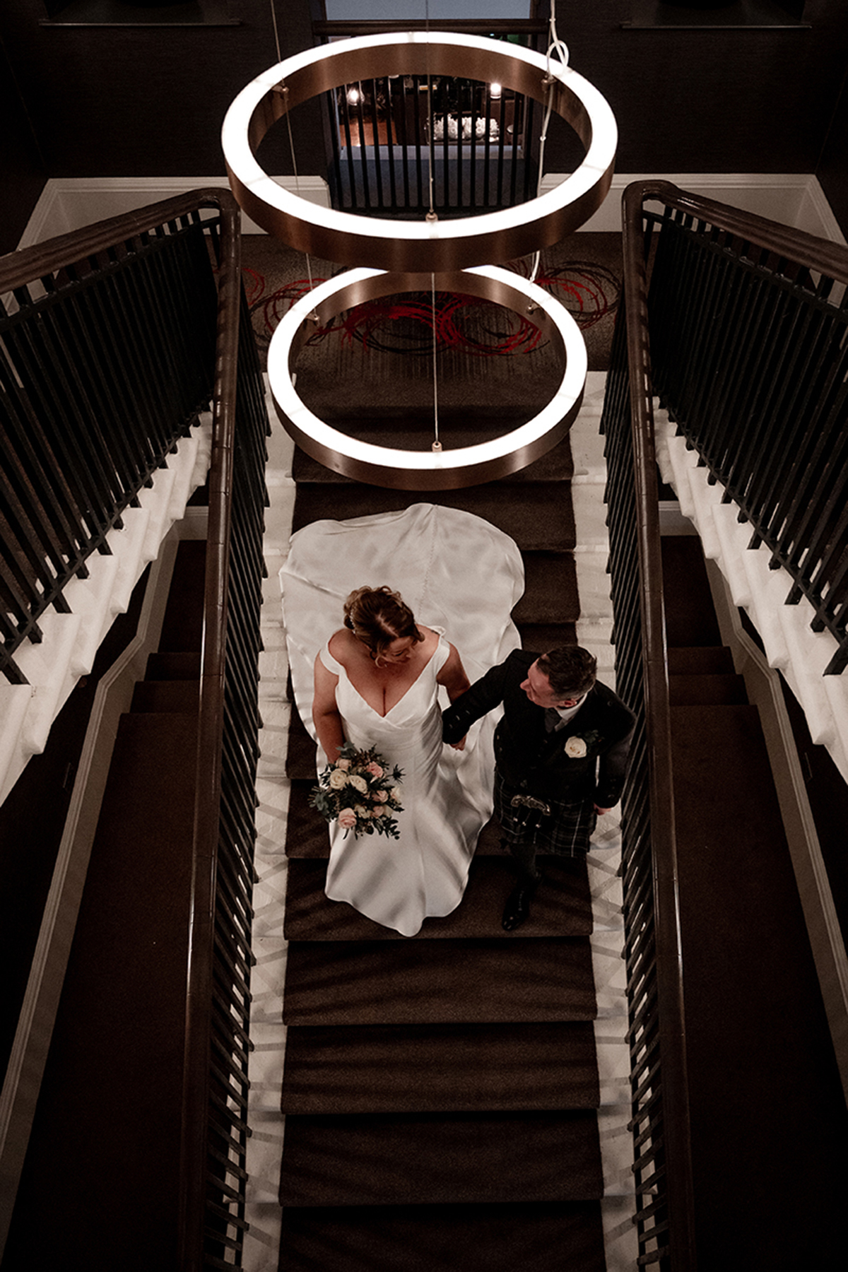Overhead view of bride and groom on staircase at Clayton Hotel Glasgow beneath statement circular lighting
