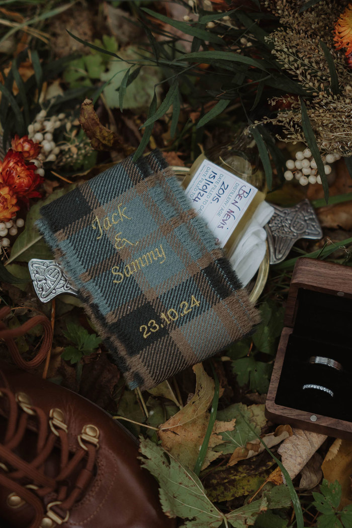 an embroidered tartan ribbon, brown hiking boots and wedding rings in a box