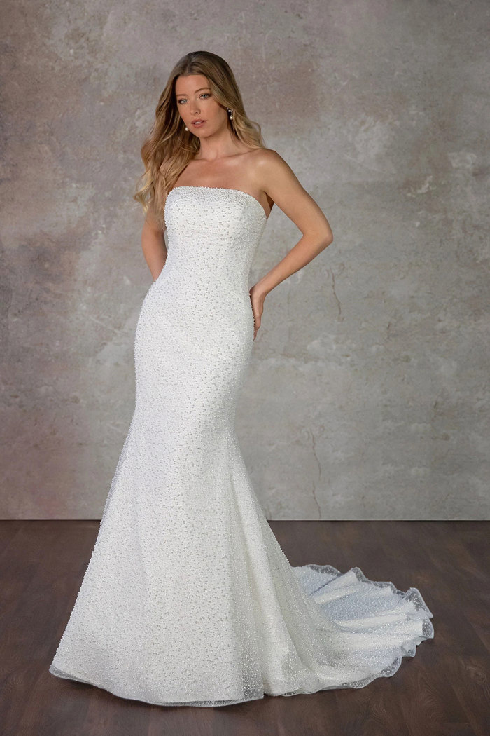 blonde model in strapless formfitting wedding dress covered in a layer of pearls standing in front of grey wall