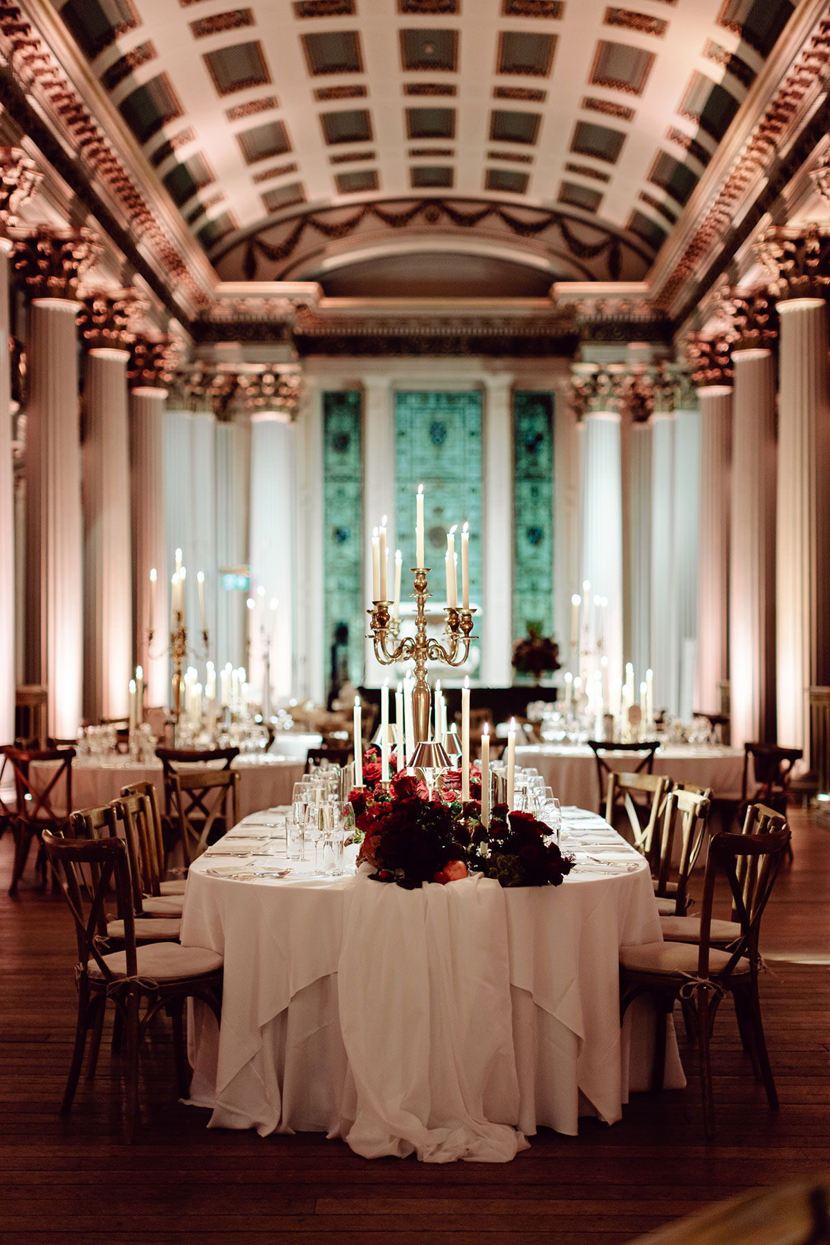 Grand reception setup at the Signet Library featuring long tables with white linens, gold candelabras and red floral centrepieces beneath ornate pillars